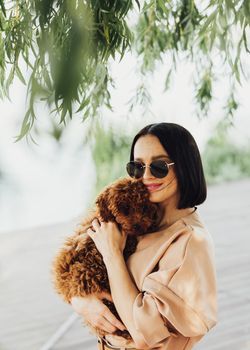Young brunette woman holding and hugging her little redhead dog breed toy poodle