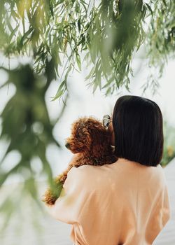 Young brunette woman holding and hugging her little redhead dog breed toy poodle