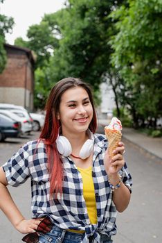 Attractive young woman in summer clothes and headphones eating ice cream at street