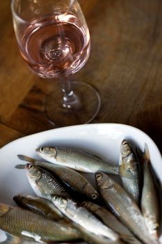 Small fresh fishes on a white plate and rose wine in a glass