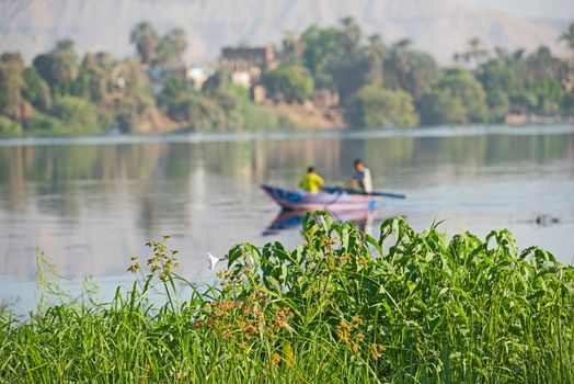 Traditional egyptian bedouin fisherman in rowing boat on river Nile fishing by riverbank