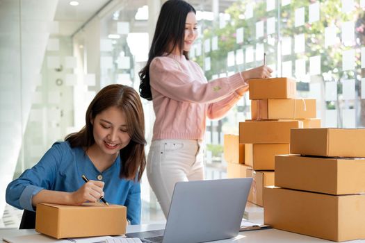 Portrait of Starting small businesses SME owners, two Asian woman check online orders Selling products working with boxs freelance work at home office, sme business online small medium enterprise.