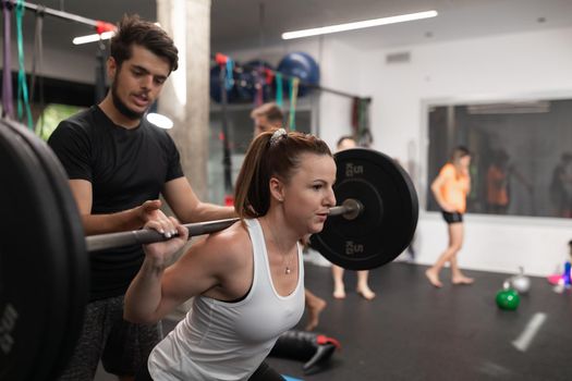 A female trainee lifting weights while being guided by her coach at the gym