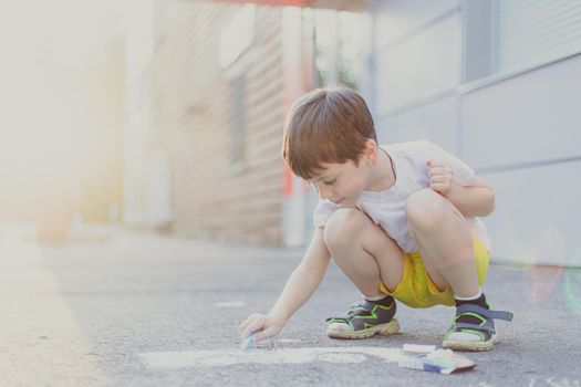 A boy draws a lifestyle with crayons on the asphalt . Children's classes. Children's drawings. Child psychology. Advertising of children's products