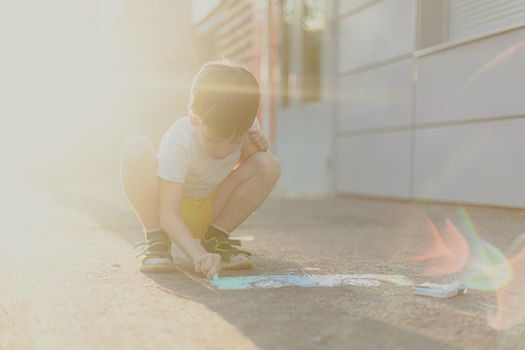 A boy draws a lifestyle with crayons on the asphalt . Children's classes. Children's drawings. Child psychology. Advertising of children's products