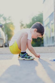 A boy draws a lifestyle with crayons on the asphalt . Children's classes. Children's drawings. Child psychology. Advertising of children's products