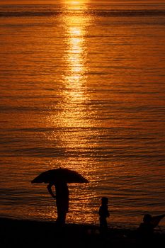 Man silhouette standing under umbrella at the sea beach. Beautiful view of orange sunset seascape. Summer resort family vacation