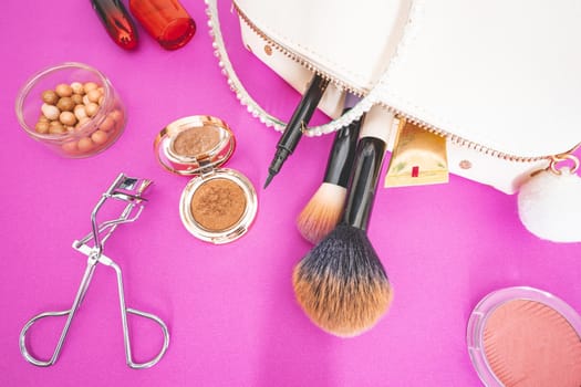Flatlay of make up and beauty products on a pink background.