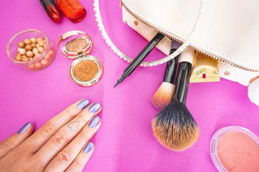 Flatlay of make up and beauty products on a pink background.