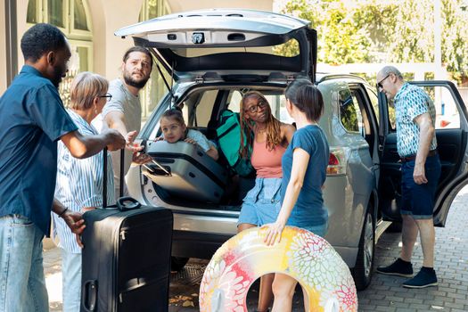 Diverse family and friends leaving on holiday, preparing vehicle with bags and luggage to go on summer vacation. Multiethnic people travelling on journey adventure with baggage in automobile.