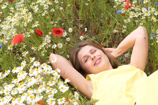 a beautiful young blonde woman in a yellow dress stands among a flowering field of poppies, daisies, cornflowers and laughs. High quality photo