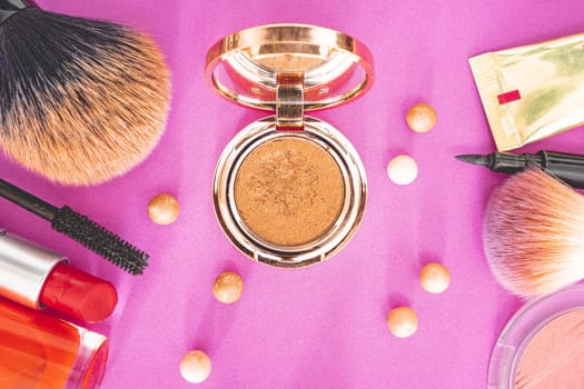 Flatlay of make up and beauty products on a pink background.