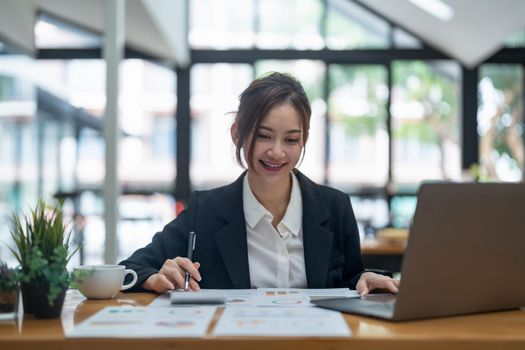 Business woman accountant calculate business report and marketing data, financial graph while working on laptop computer with spreadsheet on office desk