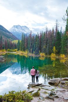 Horseshoe lake Jasper Canadian Rockies Alberta Canada, colorful autumn trees reflected in the lake. Couple Asian women and caucasian men on vacation in Canada standing by a lake with autumn trees