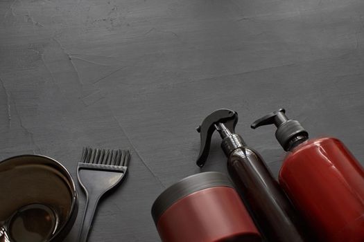 Top view of a professional hairdresser kit with copy space on a black background. Coloring brush, plastic bowl and barbers hair care products. Branding mockup.