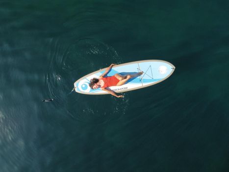 Young attractive brunette woman in red swimsuit, swimming on kayak around volcanic rocks, like in Iceland. Back view. Christmas holiday vacation and travel concept.