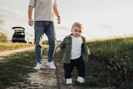 Funny Toddler Boy Trying to Walk Without Help from His Father Outdoors on Country Road