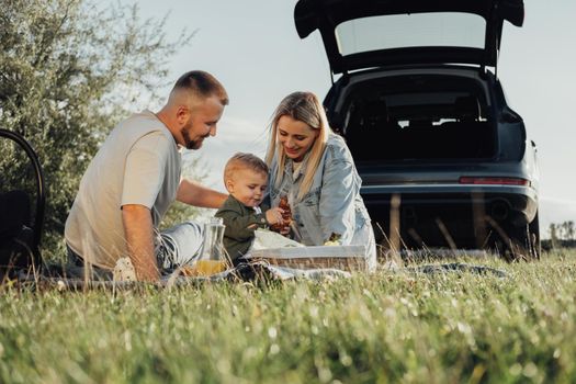 Happy Young Family, Mom and Dad with Toddler Son Having Picnic Outdoors, Weekend Road Trip by the Car
