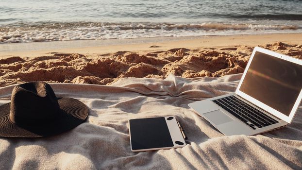 Close Up View of Laptop, Tablet and Hat Lying on the Plaid on Sandy Beach by Sea, Freelance Concept, Remote Working