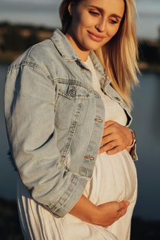 Close Up Portrait of a Pregnant Young Caucasian Woman Holding Her Belly at Sunset Outdoors