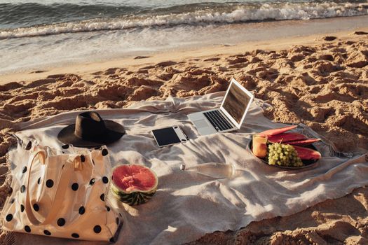 Laptop with Tablet and Fruits Lying on Plaid on Sandy Beach, Picnic Set by Sea