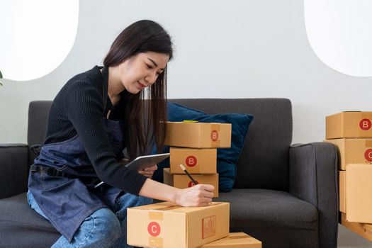 Young woman entrepreneur and business owner, working in a workshop. Packaging cardboard boxes for sending products to an online store.