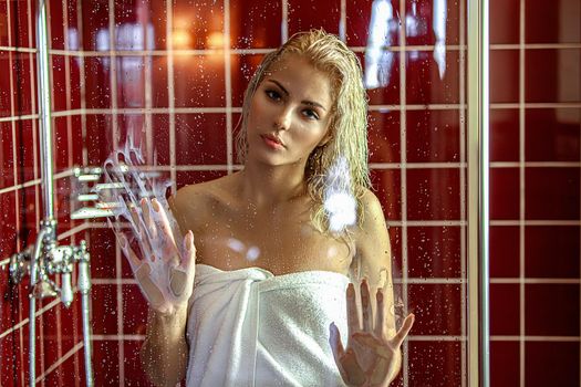 Portrait of a beautiful attractive sexy and sensuality young adult pretty blonde woman in bath relaxing behind the glass with a towel