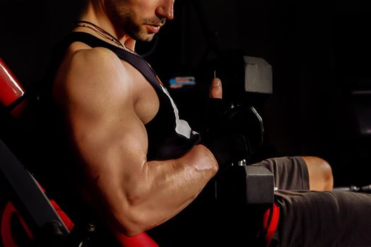 Close up portrait of a fit young man working out with steel dumbbells on dark backdrop.