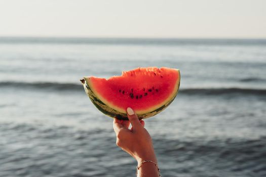 Woman's Hand Holding Piece of Watermelon on the Background of the Sea