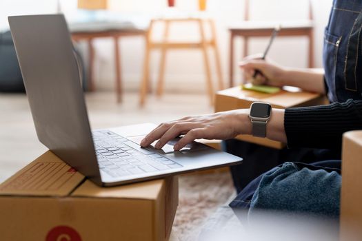 startup small business owner writing address on cardboard box at workplace. Freelance Asian woman small business entrepreneur SME working with box at home