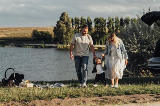 Mother and Father Help Their Toddler Son Take the First Steps, Family Picnic Outdoors by Lake