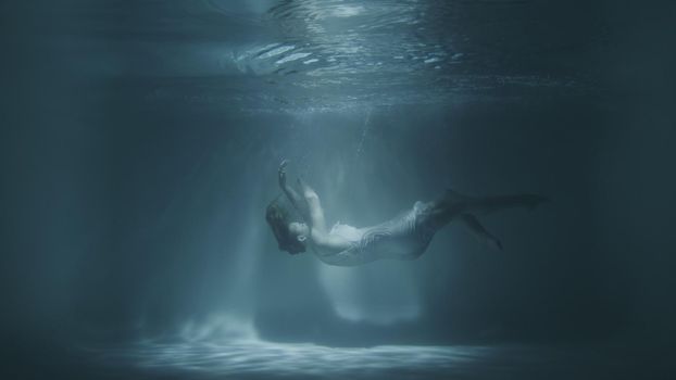 a girl in a white dress falls under the water in 4k