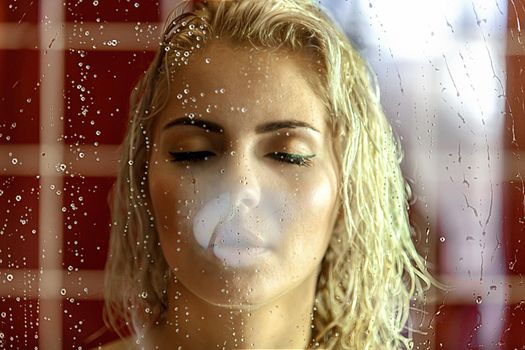 Portrait of a beautiful attractive sexy and sensuality young adult pretty blonde woman in bath relaxing behind the glass