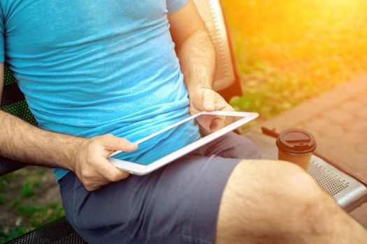 Man sitting on a bench and using a digital tablet. Men's hands closeup. Sun flare