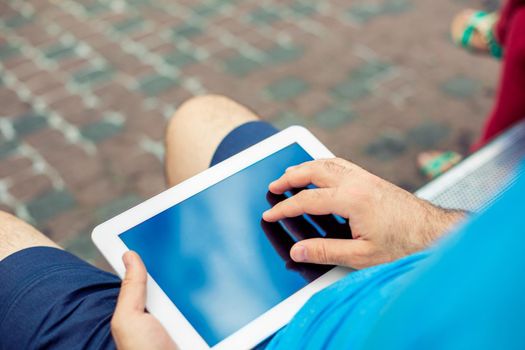 Man sitting on a bench and using a digital tablet. Men's hands closeup