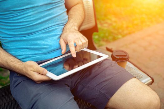 Man sitting on a bench and using a digital tablet. Men's hands closeup. Sun flare