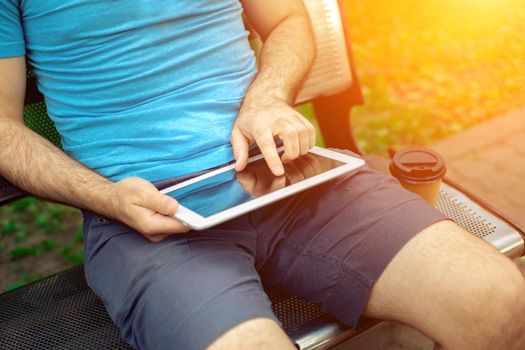 Man sitting on a bench and using a digital tablet. Men's hands closeup. Sun flare