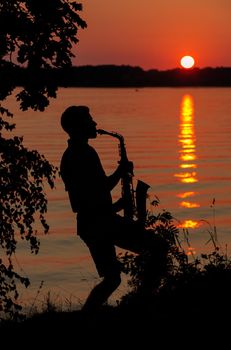 Silhouette of a young guy playing the saxophone in the evening at sunset.