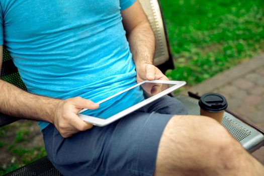 Man sitting on a bench and using a digital tablet. Men's hands closeup