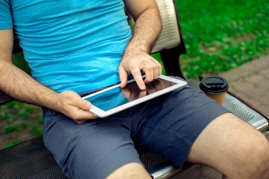 Man sitting on a bench and using a digital tablet. Men's hands closeup