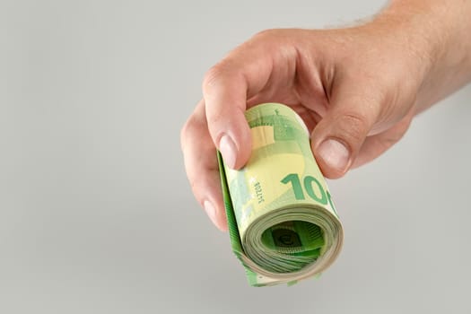 The hand holds a roll of 100 euro banknotes. Euro banknotes rolled up in a white man's hand on a gray background. The concept of financial assistance, real estate purchase, loan or insurance payment