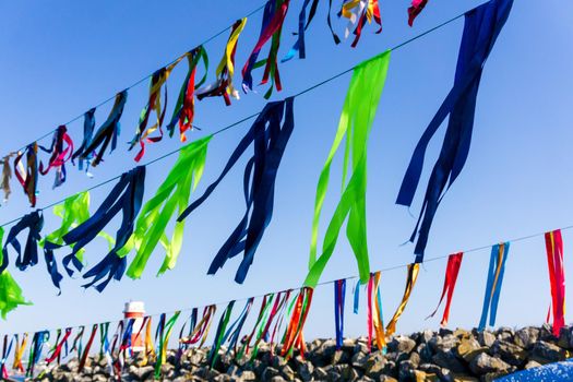 Festive garlands of multi-colored ribbons against the sky with a breakwater and a lighthouse