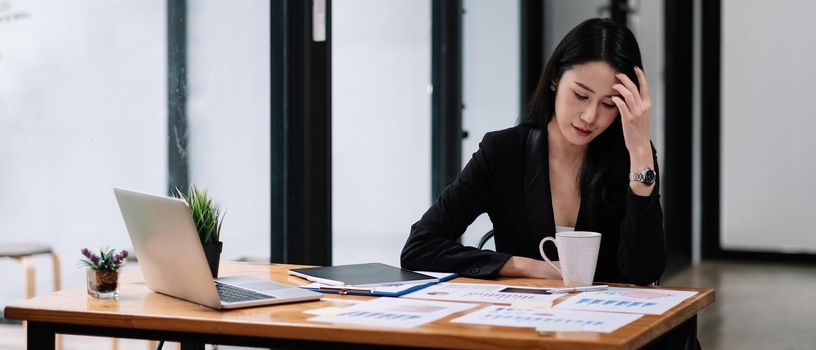 Young asian businesswoman sitting at workplace and working with marketing report.