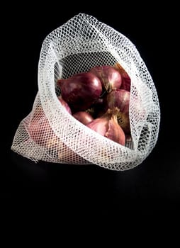 Red onions in mesh bag and some on floor isolated on black background