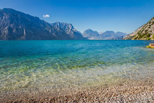Idyllic lake Garda coastline in Malcesine with translucent water and mountains, Northern Italy