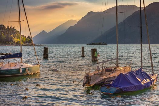 Idyllic lake Garda coastline and mediterranean village of Torbole with sailboats and mountains, Northern Italy