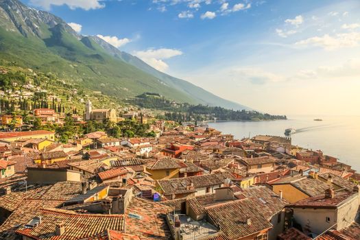 Lake Garda above Malcesine old town with motorboat at golden sunrise and mountain range