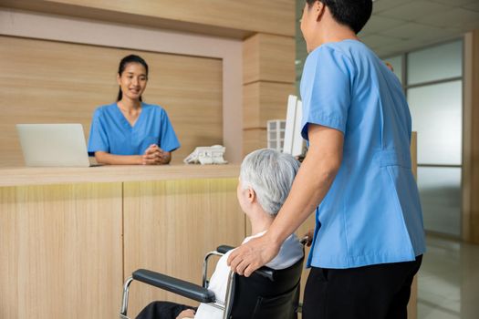 Patient elderly sit on wheelchair meet and talking with nurse or staff at front counter in of the hospital, healthcare reception service treatment process concept