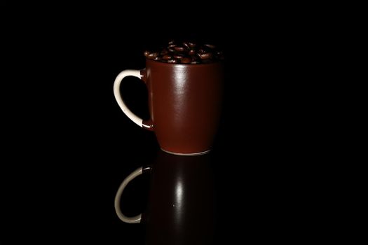 Coffee beans lie in dark brown mugs, on a black background. Isolated. Roasted coffee seeds. Close-up.