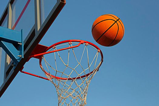 A basketball in a net on a blue sky background. The ball hit the ring. Sports, team game. Conceptual: victory, success, hitting the target, sport.